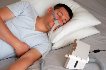 Close-up of young adult man wearing under the nose nasal mask ( CPAP mask ) and using CPAP machine...