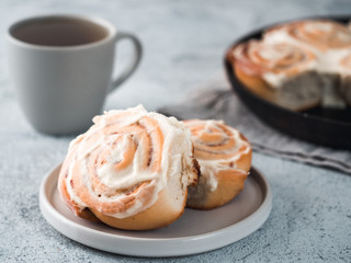 Obraz na płótnie Canvas Vegan swedish cinnamon buns Kanelbullar with pumpkin spice,topping vegan cream cheese in plate with tea cup on table. Idea and recipe pastries - perfect cinnamon rolls. Copy space. Shallow DOF