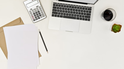 Modern white office desk table with laptop, calculator, paper, coffee cup, pencil and cactus on white background. Top view.