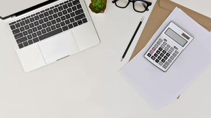 Modern white office desk table with laptop, calculator, paper, eye glasses, pencil and cactus on white background. Top view.