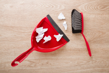 Red broom and dustpan with paper on wooden floor. Closeup. Top down view.