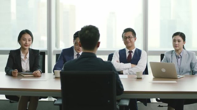 rear view of a young asian businessman being interviewed by a group of HR executives in conference room of modern corporation