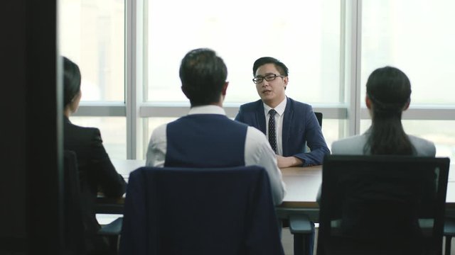 arrogant young asian business man being interviewed by a group of HR executives in conference room of modern corporation