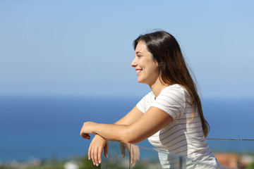 Happy woman looking away in a balcony on the beach