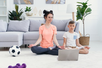 Mom and son practice yoga with laptop on the floor. Sporty mother with children exercising in the morning at home.