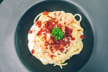 Spaghetti white sauce with bacon served on black dish in the cafe.