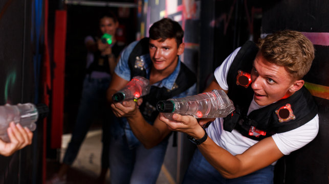 Portrait of positive friends standing with laser guns during laser tag game in dark room