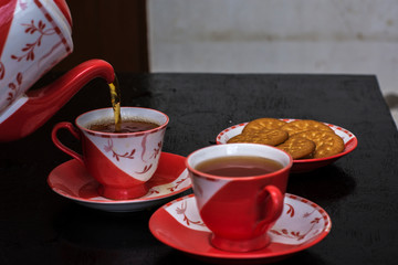 Pouring tea into ceramic cup on a wooden table with some biscuit on plate.