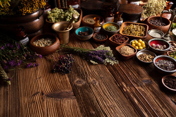 Natural medicine background. Assorted dry herbs in bowls and brass mortar on rustic wooden table.