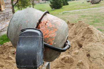 a dirty concrete mixer stands in close-up against a blurry background of nature