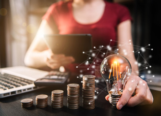 Businessman hand holding lightbulb with using laptop computer and money stack in office. idea saving energy and accounting finance concept.