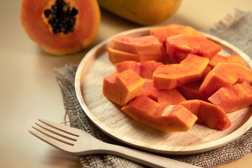 Wooden dish of fresh papaya fruit slices (papaw or pawpaw) contain vitamin A, C and fibre on hessian or burlap with plain yellow background. Healthy food ready to eat concept