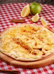 Rustic pizza with cheese, apple and cinnamon served on a wooden board for a dinner in italian restaurant background. Fruit dessert pizza