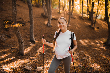 Portrait of young happy pregnant woman nordic walking in autumn forest with backpack and trekking...