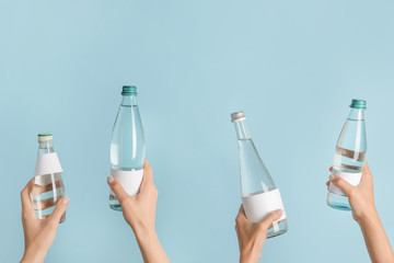 Hands with bottles of clean water on color background