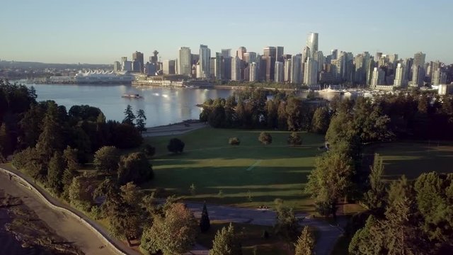 The Lush Green Trees At Brockton Point Of Stanley Park Overlooking The Downtown Skyline Of Vancouver And Coal Harbour During A Beautiful Sunrise In British Columbia, Canada. - aerial drone