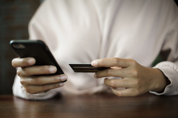Close up of a teenage woman holding credit card and smart phone make online payment. Stock photo.