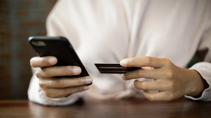 Close up of a teenage woman holding credit card and smart phone make online payment. Stock photo.