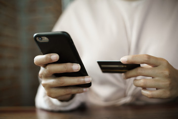 Close up of a teenage woman holding credit card and smart phone make online payment. Stock photo.