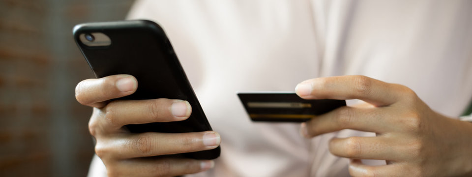 Close up of a teenage woman holding credit card and smart phone make online payment. Stock photo.