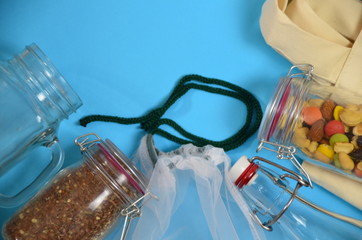 Plastic free, zero waste shopping and living. Reusable, recycled, homemade produce bag for fruit or vegetables, a textile bag, a stainless steel bottle, cereals and nuts in a glass jar on blue
