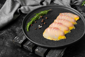 Cold-smoked sturgeon. Slices of sturgeon fish in a black ceramic plate on a black kitchen table