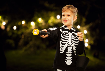 halloween, holiday and childhood concept - happy boy in black costume of skeleton with bucket of...