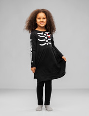 Obraz premium halloween, holiday and childhood concept - smiling african american girl in black costume dress with skeleton bones over grey background