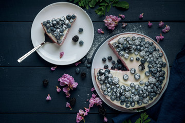 Piece of cottage cheese casserole with cake server. Cheese pie decorated with blackberry, blueberry and mint leaves on dark wooden table. Flat lay.