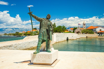 Old stone bridge and city gates with monument of medieval Croatian duke in the town of Nin in...