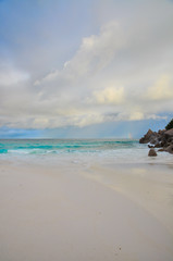 Tropical withe beach with granite rocks and cloudy stormy sky. Petite Anse, La Digue Island, Seychelles