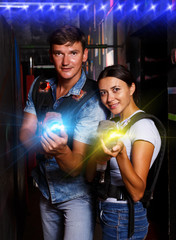 Smiling couple holding colored laser guns during laser tag game in labyrinth