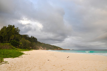 Tropical withe beach with granite rocks and cloudy stormy sky. Petite Anse, La Digue Island, Seychelles