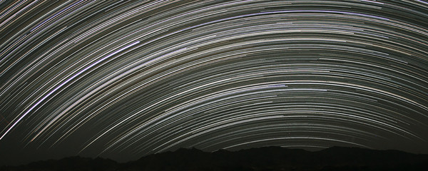 Night glowing stars trails in the sky. Silhouettes of mountains range. Long exposure