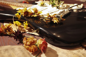 Dried flowers on electric guitar and vintage music notes close up.