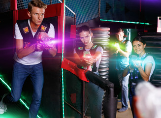 Obraz na płótnie Canvas Portrait of positive glad young friends standing with laser guns during laser tag game in dark room