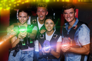 Emotional young people standing with laser guns having fun together in dark labyrinth