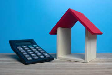 Selective focus of small wooden house and calculator on wooden table with a blue background.