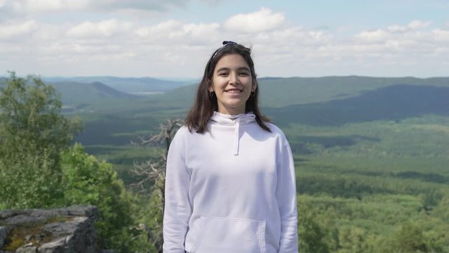 Portrait of a smiling girl standing on top of a mountain, looking in the camera.