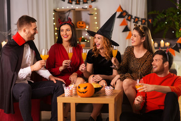 friendship, holiday and people concept - group of happy smiling friends in halloween costumes of vampire, devil, witch and cheetah with non-alcoholic drinks at home party at night