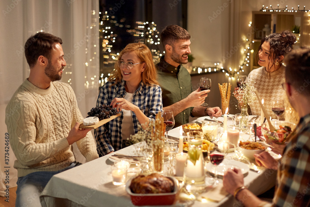 Wall mural holidays, celebration and people concept - happy smiling friends having christmas dinner party at home in evening