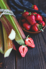 Fresh organic garden strawberries and rhubarb stems on wooden background. Flat lay. Ingredients for summer lemonade, jam or cake