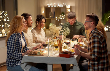 holidays, celebration and people concept - happy smiling friends having christmas dinner party at home in evening