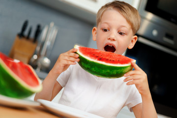 Little boy eating watermelon piece in the kitchen