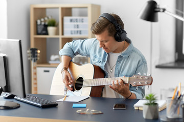 leisure, music and people concept - young man or musician in headphones playing guitar sitting at table at home