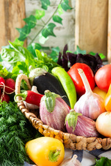 Assortment of vegetables in a basket on the table. A lot of different raw vegetables in the basket. Eggplant, tomatoes, garlic, sweet pepper, onion on the table. Healthy food concept