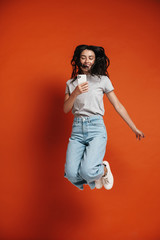 Image of young joyful woman jumping and using cellphone