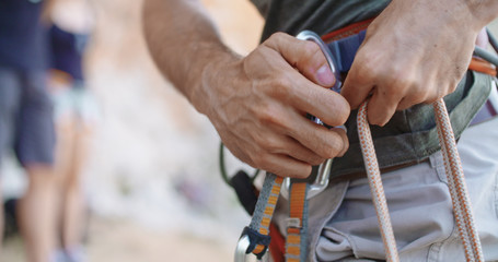 Climber man preparing for climbing up the rocky wall rift by getting carabiners. Climbing extreme active sport activity. Active people, outdoor activities. Side detail.