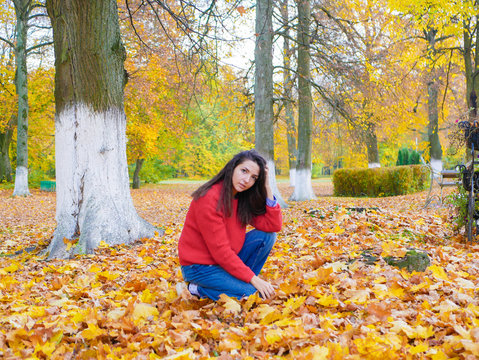 young girl sitting on yellow foliage in the park