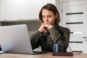 Concentrated short haired woman looking at laptop listening to webinar while sitting at home